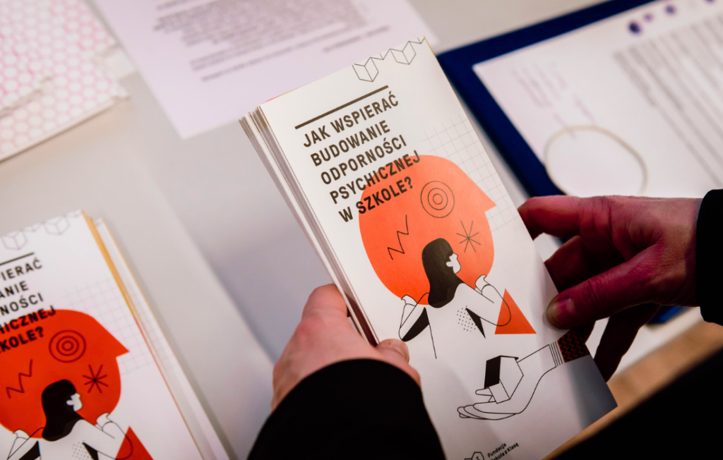 ręce kobiety sięgające po ulotkę programu szkoła z klasą o tym jak budować odporność psychiczną dzieci
